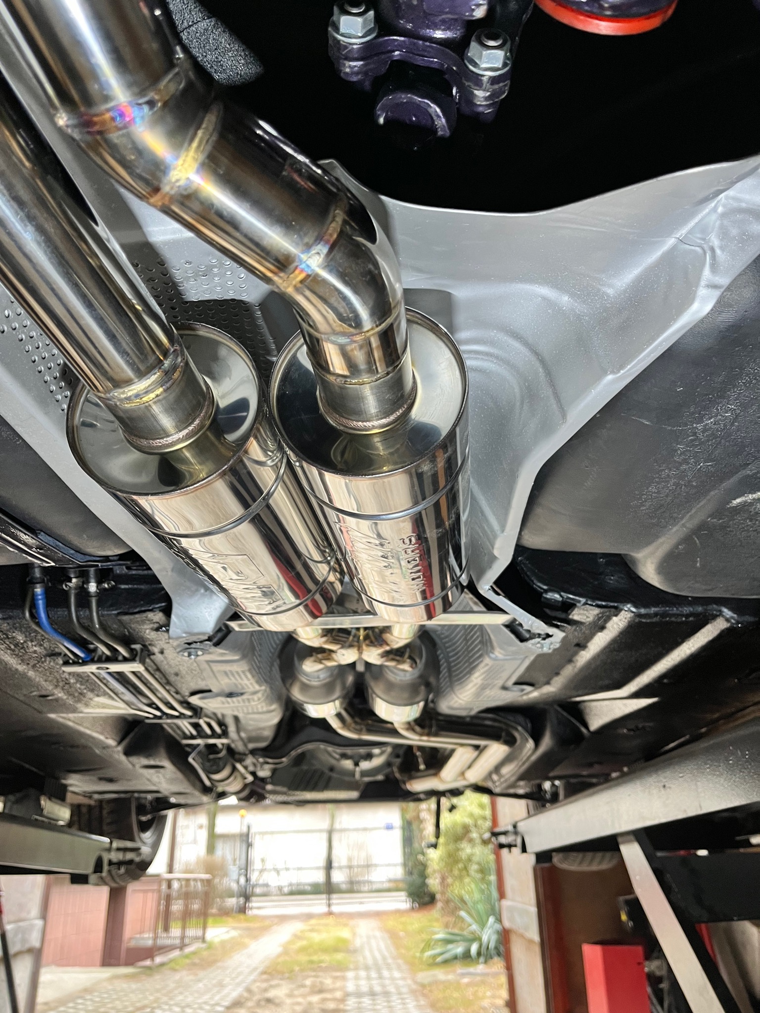 Widok od spodu na zamontowany, polerowany, nierdzewny układ wydechowy z podwójnymi końcówkami w samochodzie na podnośniku.