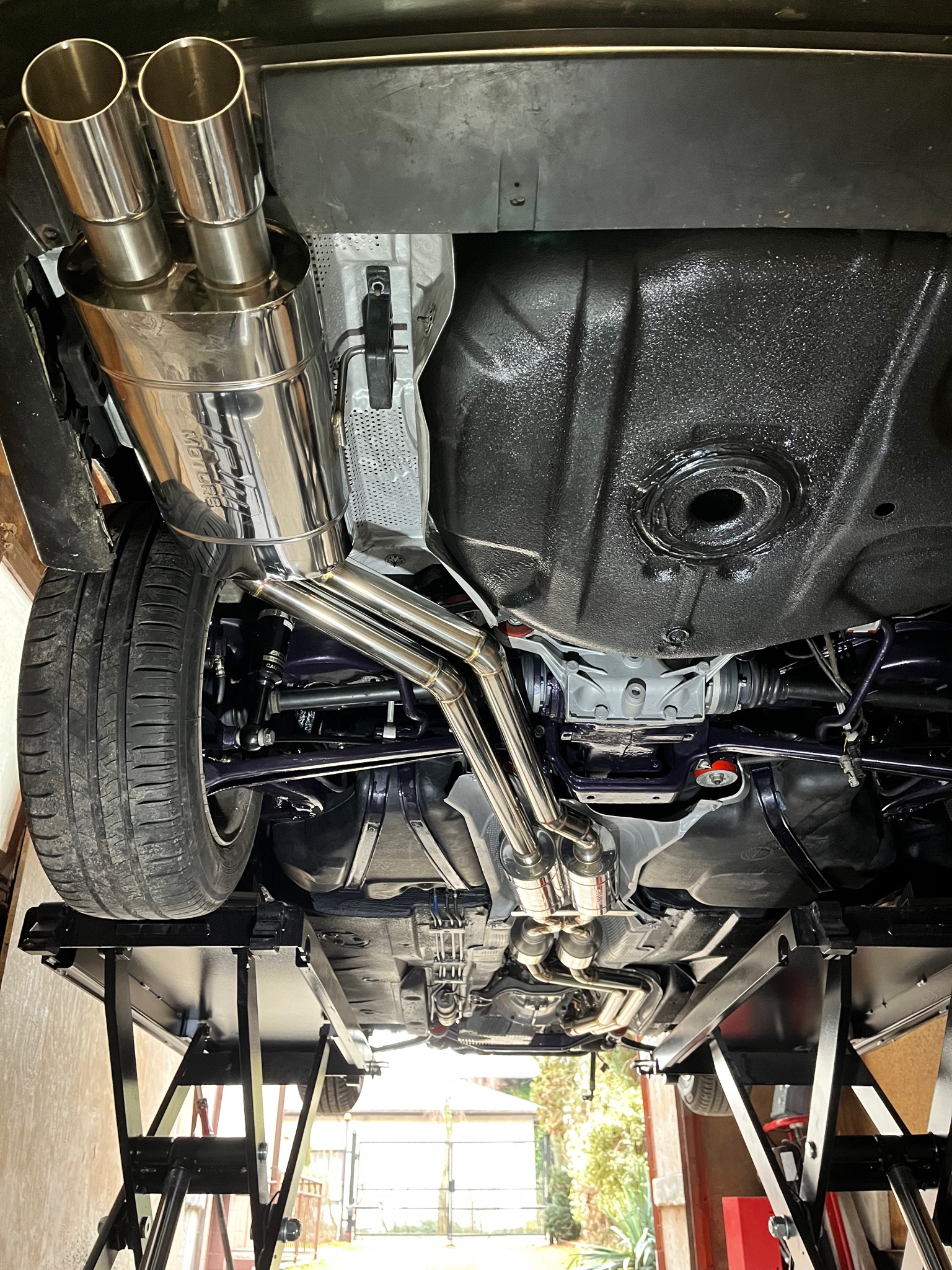 Widok od dołu na podwozie samochodu na podnośniku, z nowym, podwójnym, polerowanym układem wydechowym ze stali nierdzewnej, z widocznymi elementami zawieszenia i zabezpieczeniem antykorozyjnym...