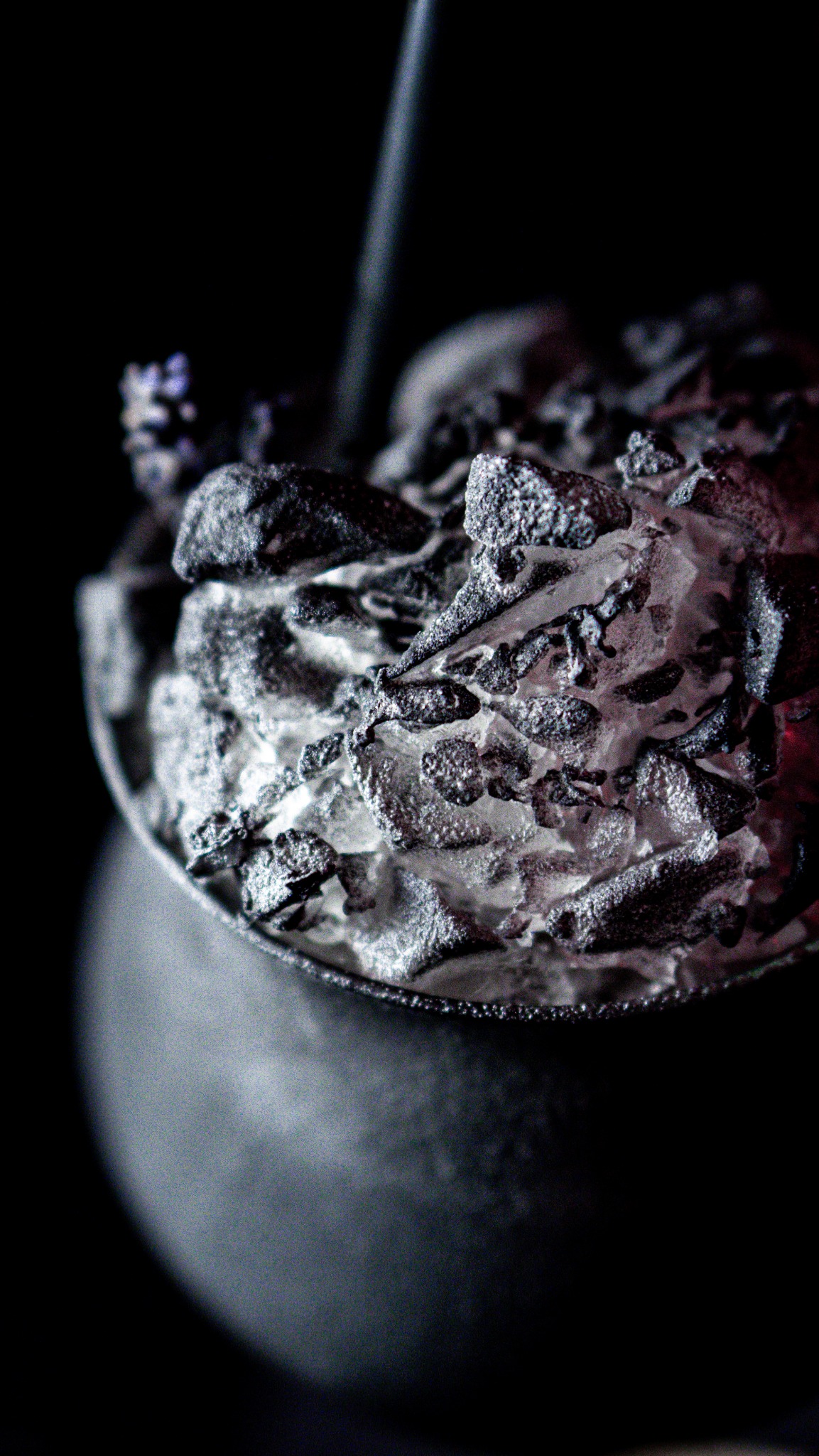 Abstrakcyjna fotografia zbliżeniowa czarnego koktajlu z dekoracją przypominającą zamsz cukierniczy w ciemnym otoczeniu.
