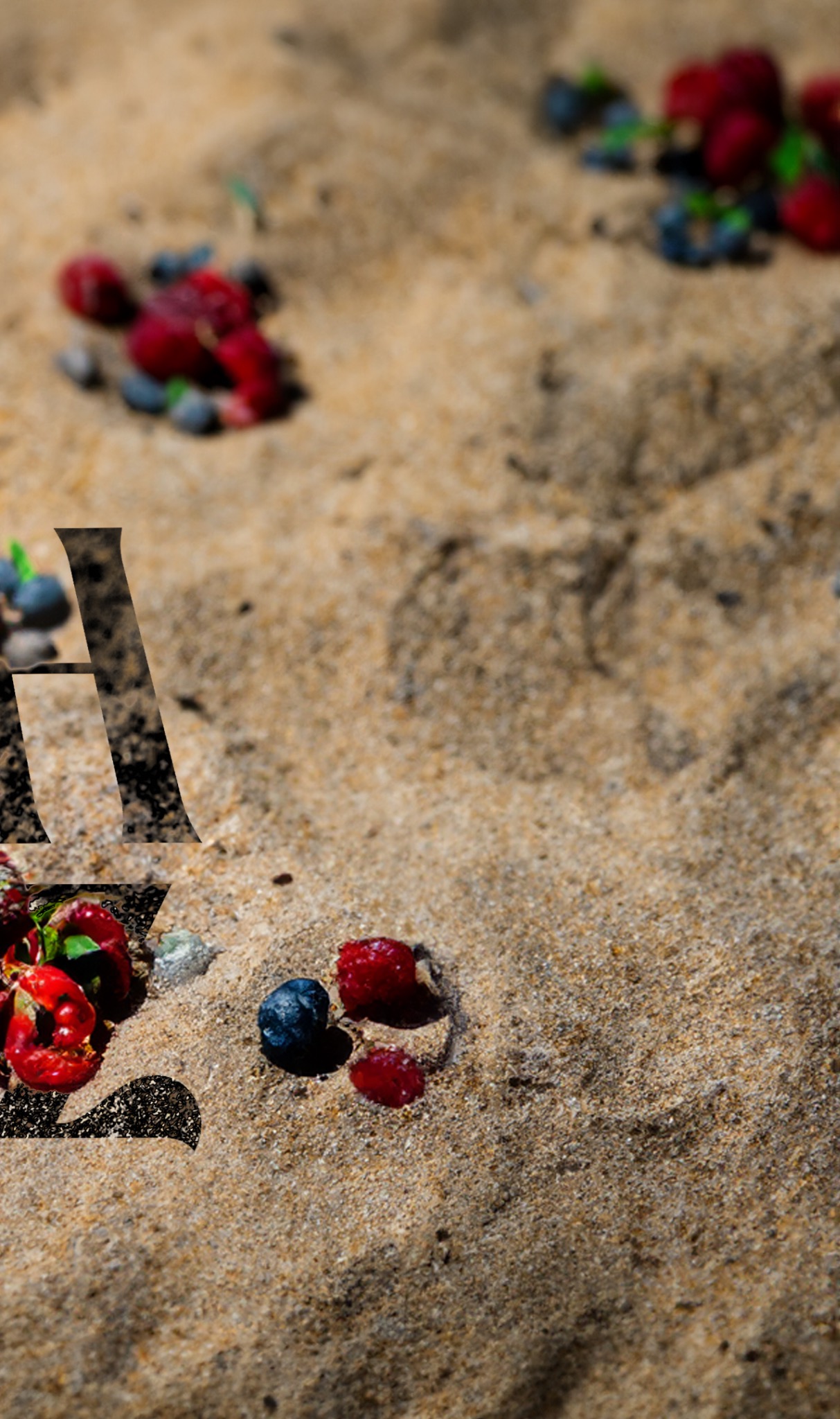 Rozrzucone maliny i jagody na piasku, z bliska, z lekkim rozmyciem tła.