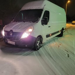 POLMAR Mariusz Kamiński - Biały bus Renault Master zaparkowany w nocy na ośnieżonej drodze, z włączonymi światłami mijania, tablica rejestracyjna widoczna, śnieg na dachu i masce pojazdu.