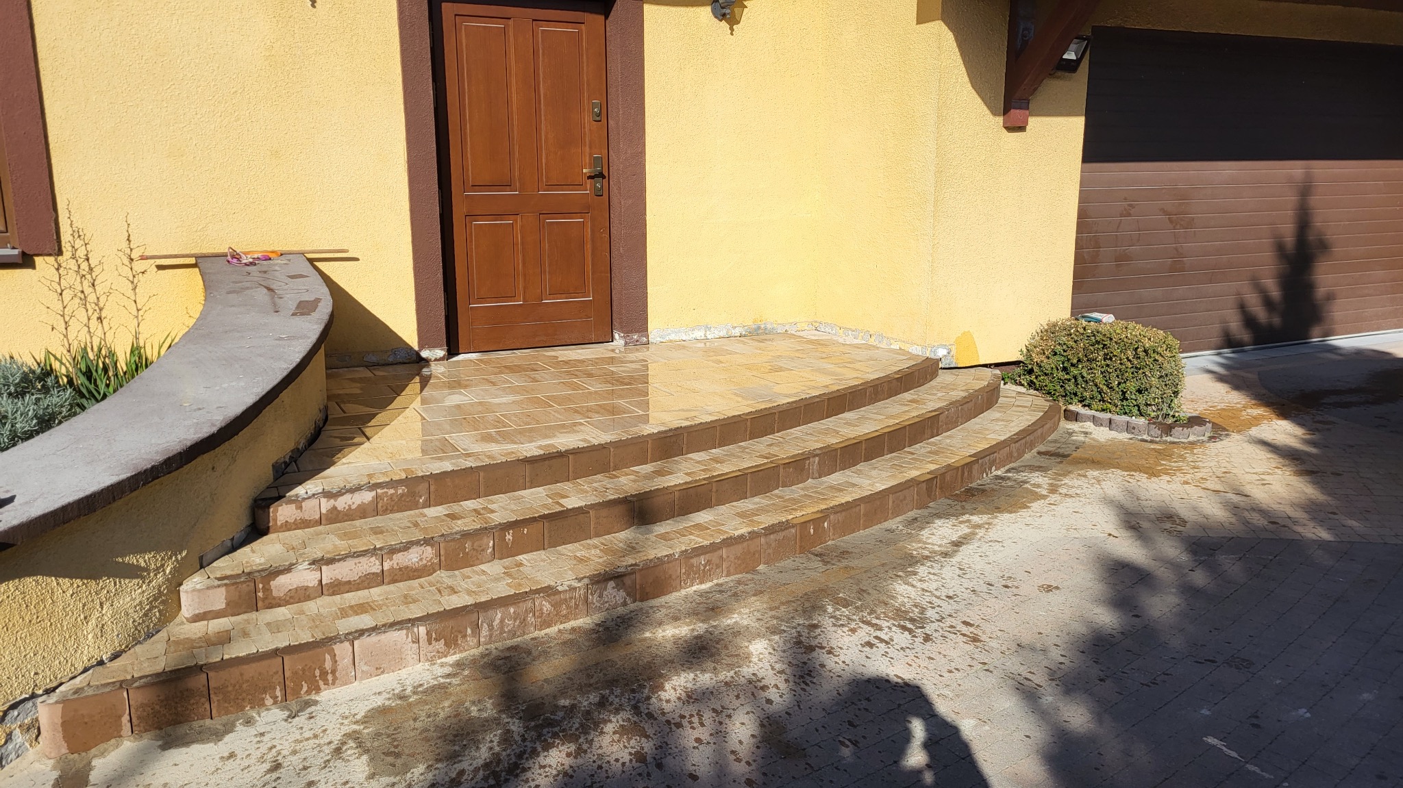 Wykończone schody wejściowe do domu z brązowej kostki, prowadzące do brązowych drzwi, z widocznymi śladami wody po myciu.