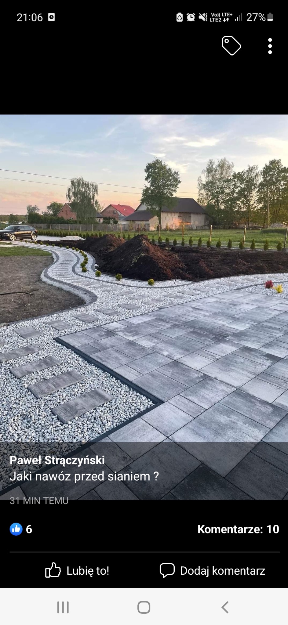 Ścieżka z płyt i grysu prowadząca przez ogród z nasadzeniami i przygotowanym podłożem pod trawnik.