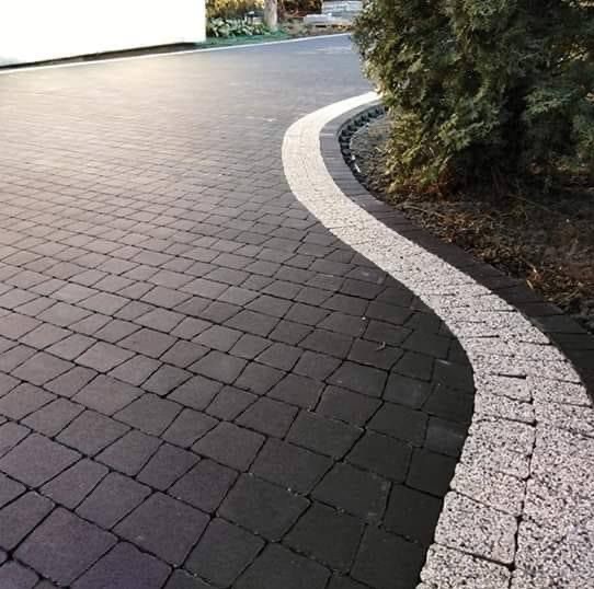 Ułożona ciemna kostka brukowa z jasnym obrzeżem tworzącym falistą linię rozgraniczającą, widok z góry.