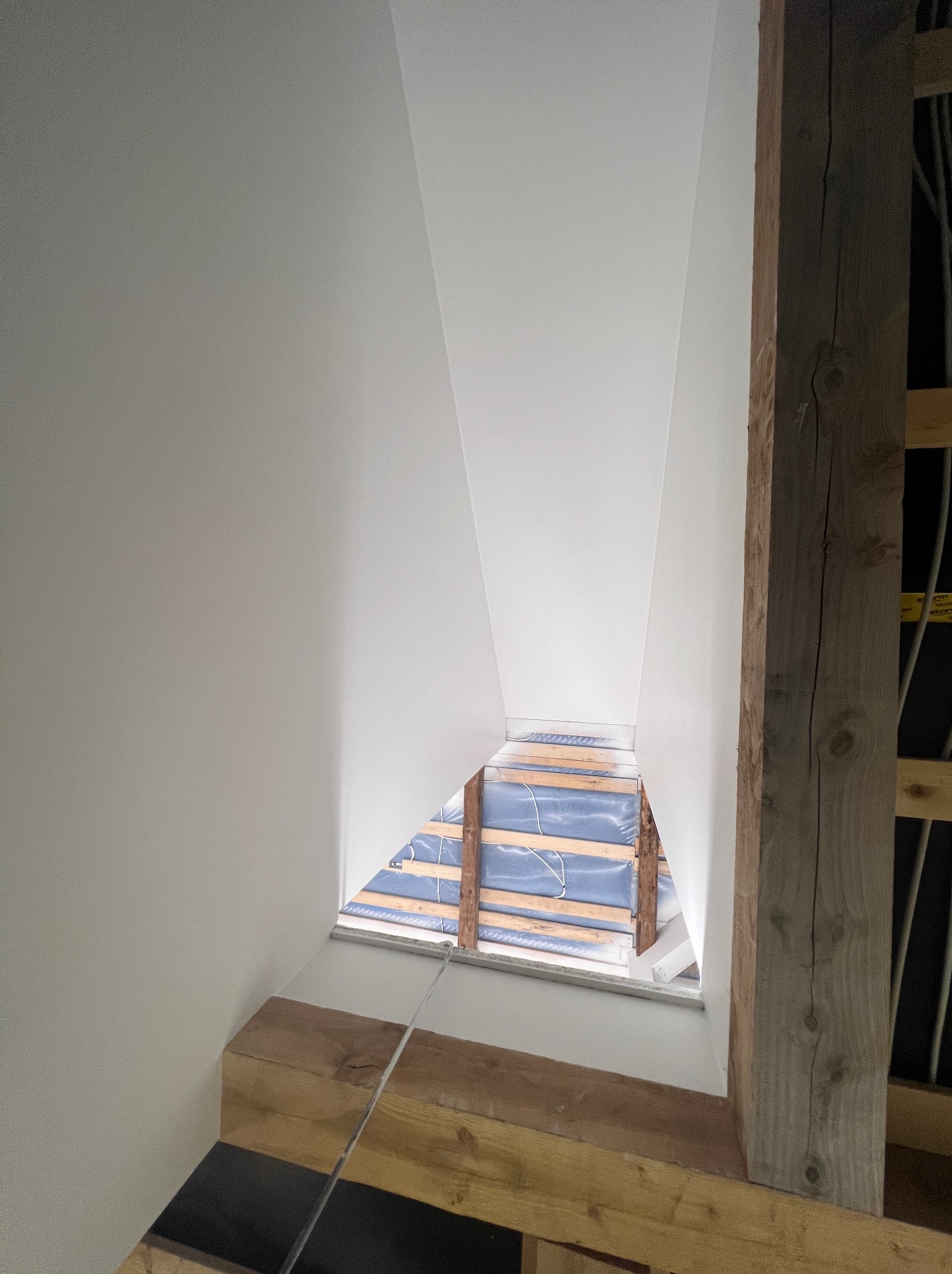 Świeżo pomalowane, białe poddasze ze skośną ścianą i drewnianą konstrukcją nośną widoczną w otworze okiennym.