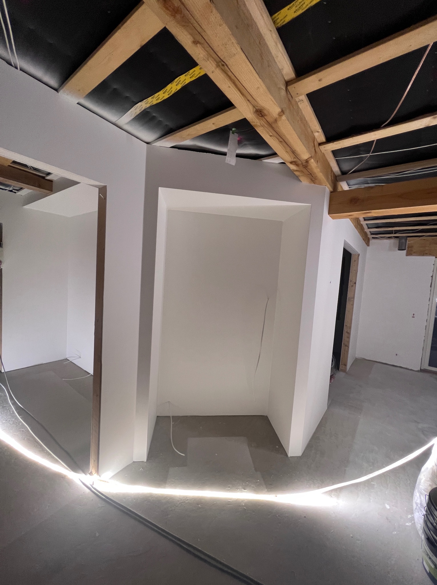 Wnętrze w trakcie wykańczania: świeżo pomalowane na biało ściany z drewnianą konstrukcją sufitu, widoczne kable i przewody, oświetlenie podłogowe.