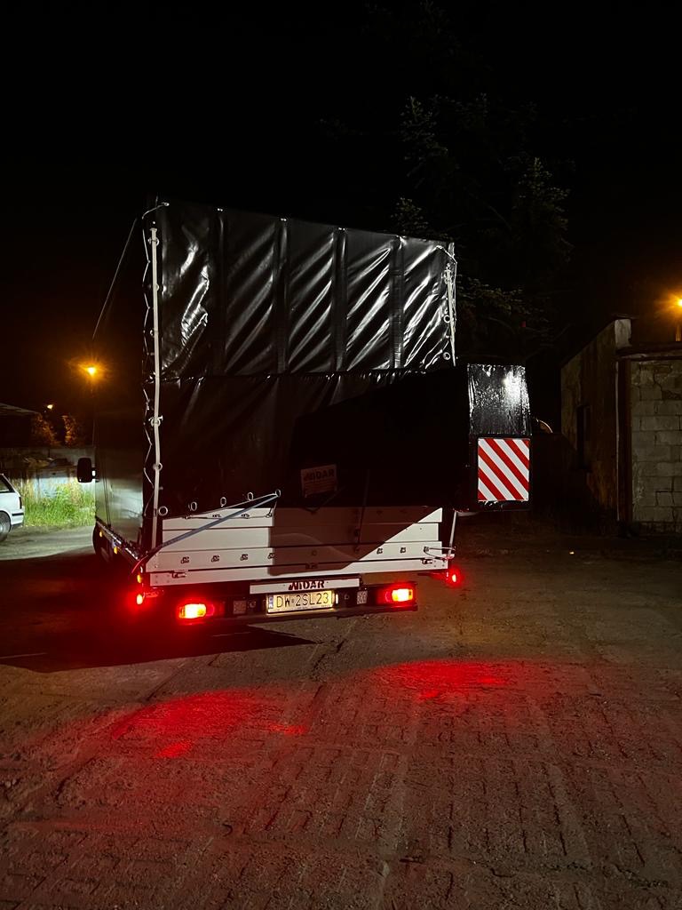 Tył busa z plandeką zaparkowanego nocą, widoczne światła stopu i tablica rejestracyjna DW 2SL23.