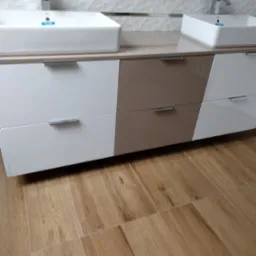 Nowoczesna łazienka w Tychach z dwoma białymi umywalkami nablatowymi i szafką pod umywalkę z frontami w kolorze białym i taupe, na podłodze płytki imitujące drewno.