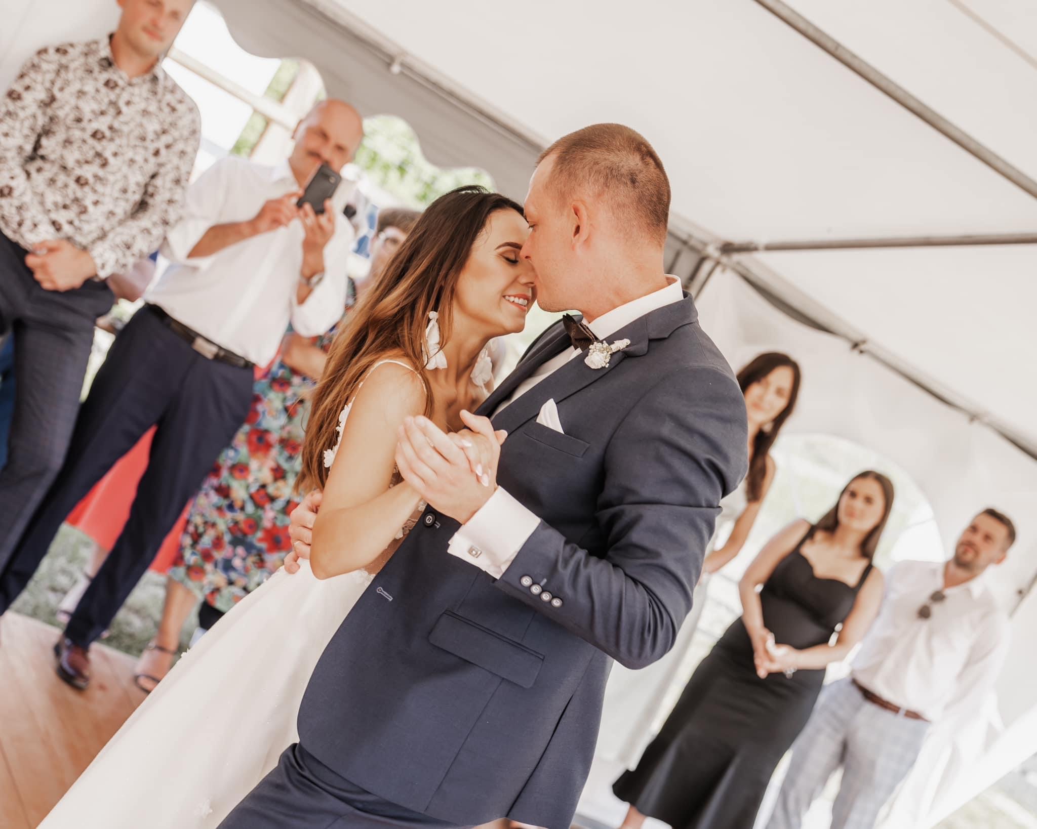 Para młoda w tańcu podczas wesela w namiocie, otoczona gośćmi robiącymi zdjęcia.