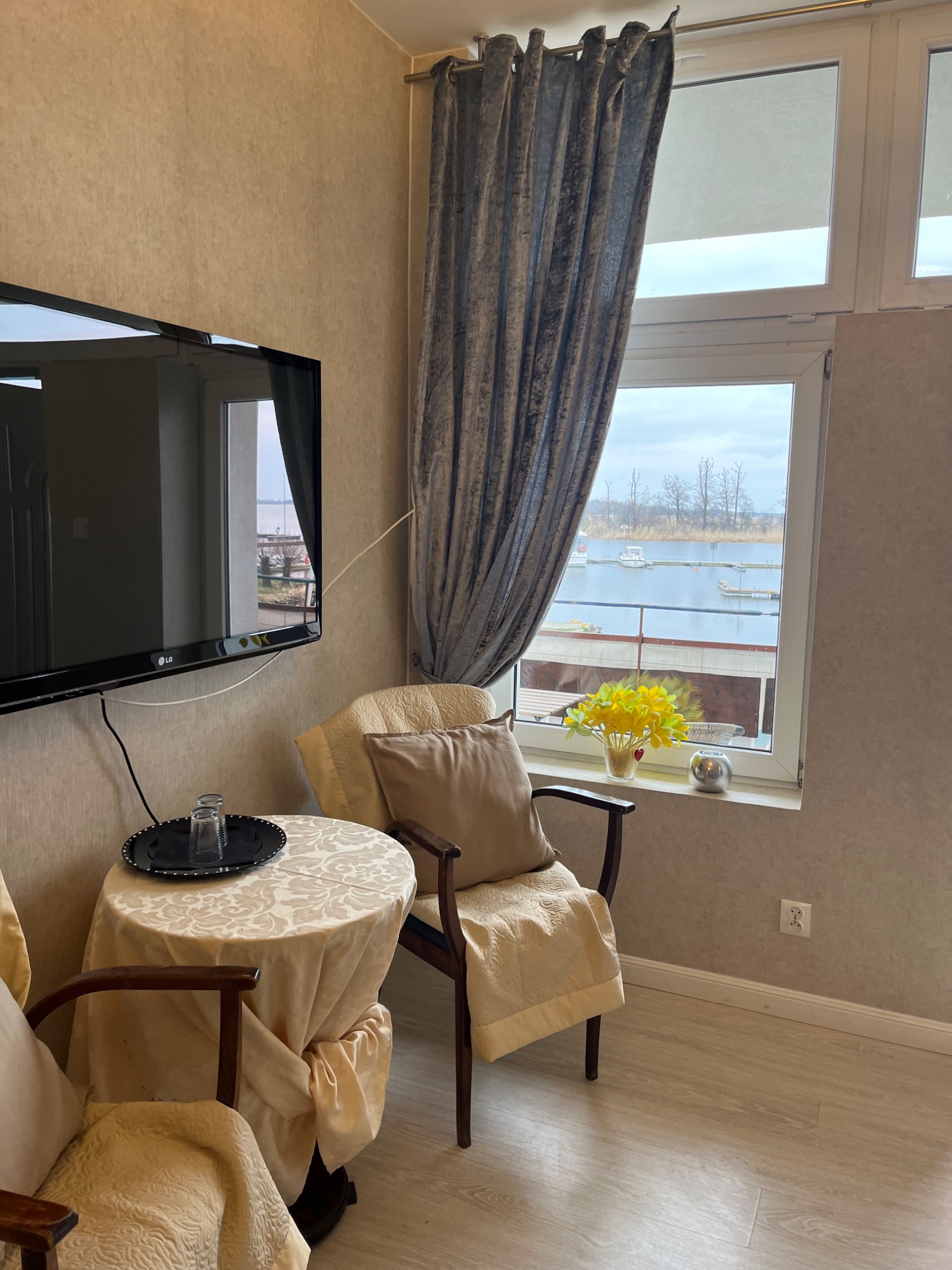 Pokój z telewizorem i widokiem na przystań jachtową przez okno, dekorowany kwiatami i nakryciem stołu w stylu vintage.