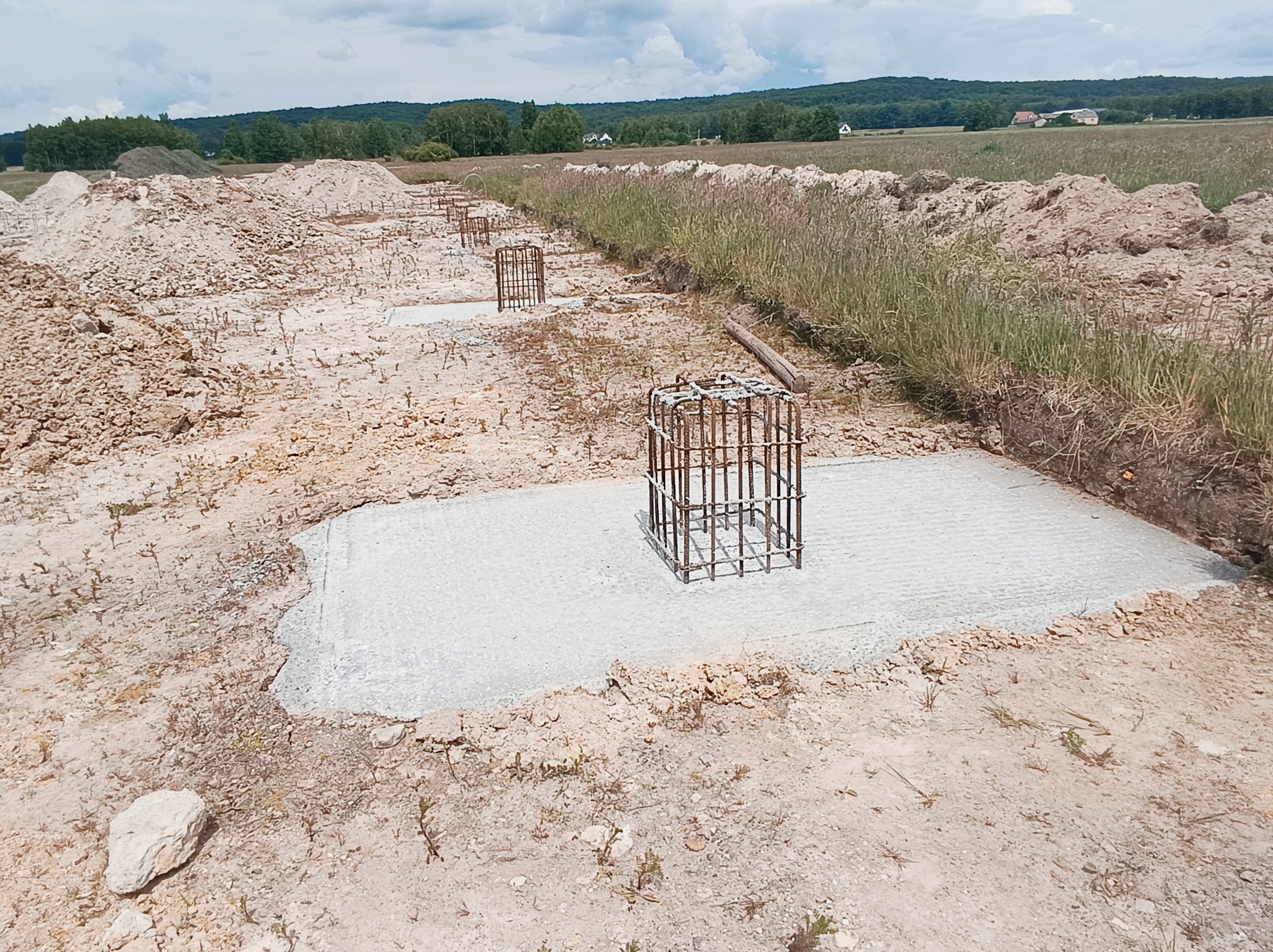 Przygotowane zbrojenie na betonowych fundamentach pod budowę domu, widok na plac budowy w słoneczny dzień.