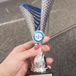 Kobieca dłoń z czerwonym manicure trzyma srebrny puchar z logo PZU, nagroda za II miejsce w kategorii Doradca aktywności za 2023 rok z wynikiem 300 ofert.