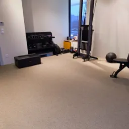 Jasny, beżowy dywan z krótkim włosiem w domowej siłowni z wyposażeniem do ćwiczeń siłowych i akcesoriami.