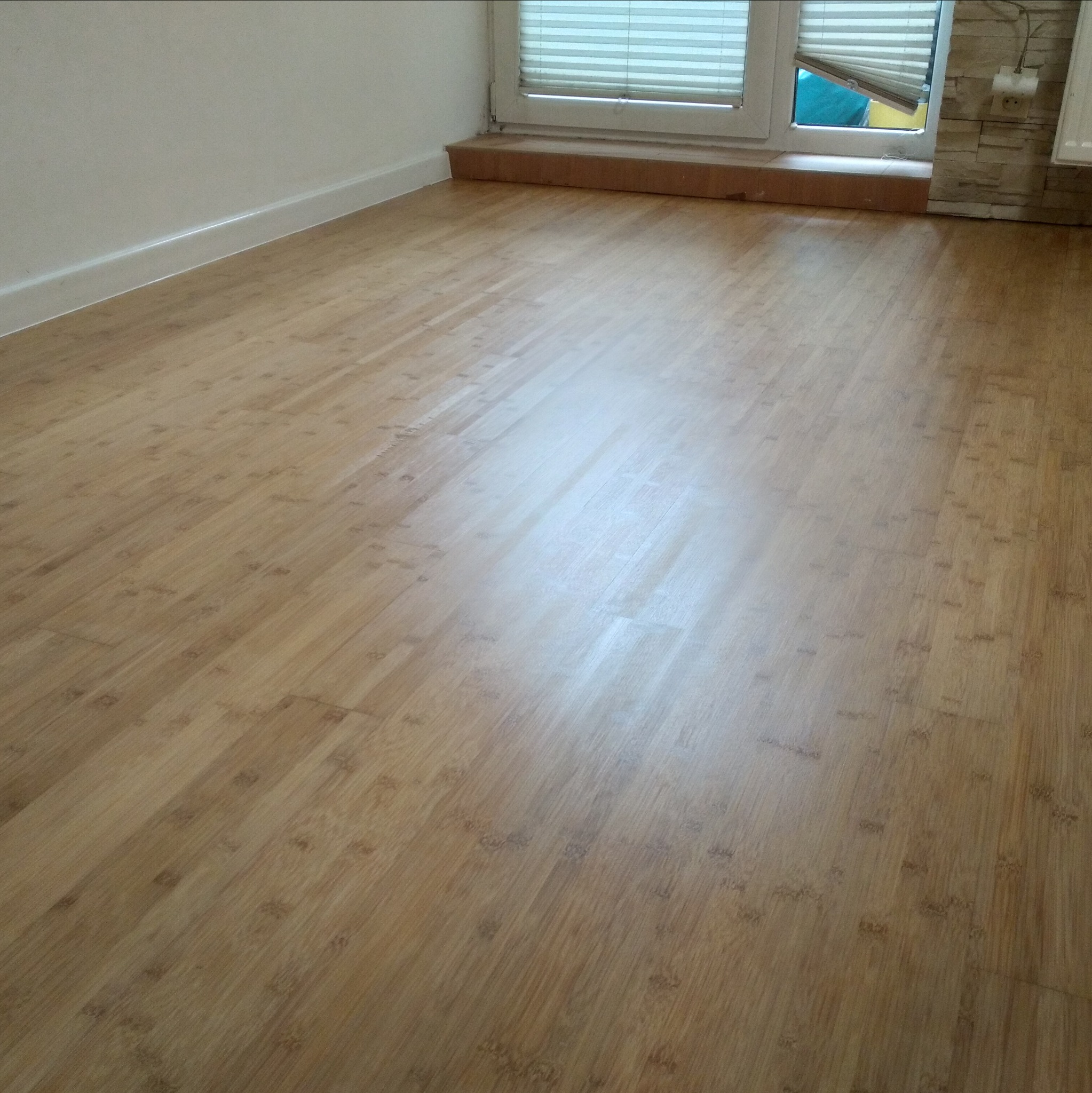 Jasna, wycyklinowana podłoga z drewna egzotycznego, widok z góry, okno z żaluzjami w tle.