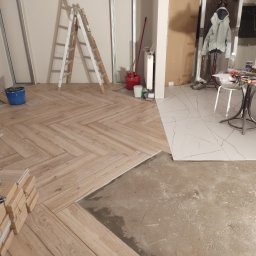 Usługi budowlane - Układanie drewnopodobnych płytek w jodełkę, widoczne narzędzia, resztki kleju i fragment podłogi z białych płytek imitujących marmur.