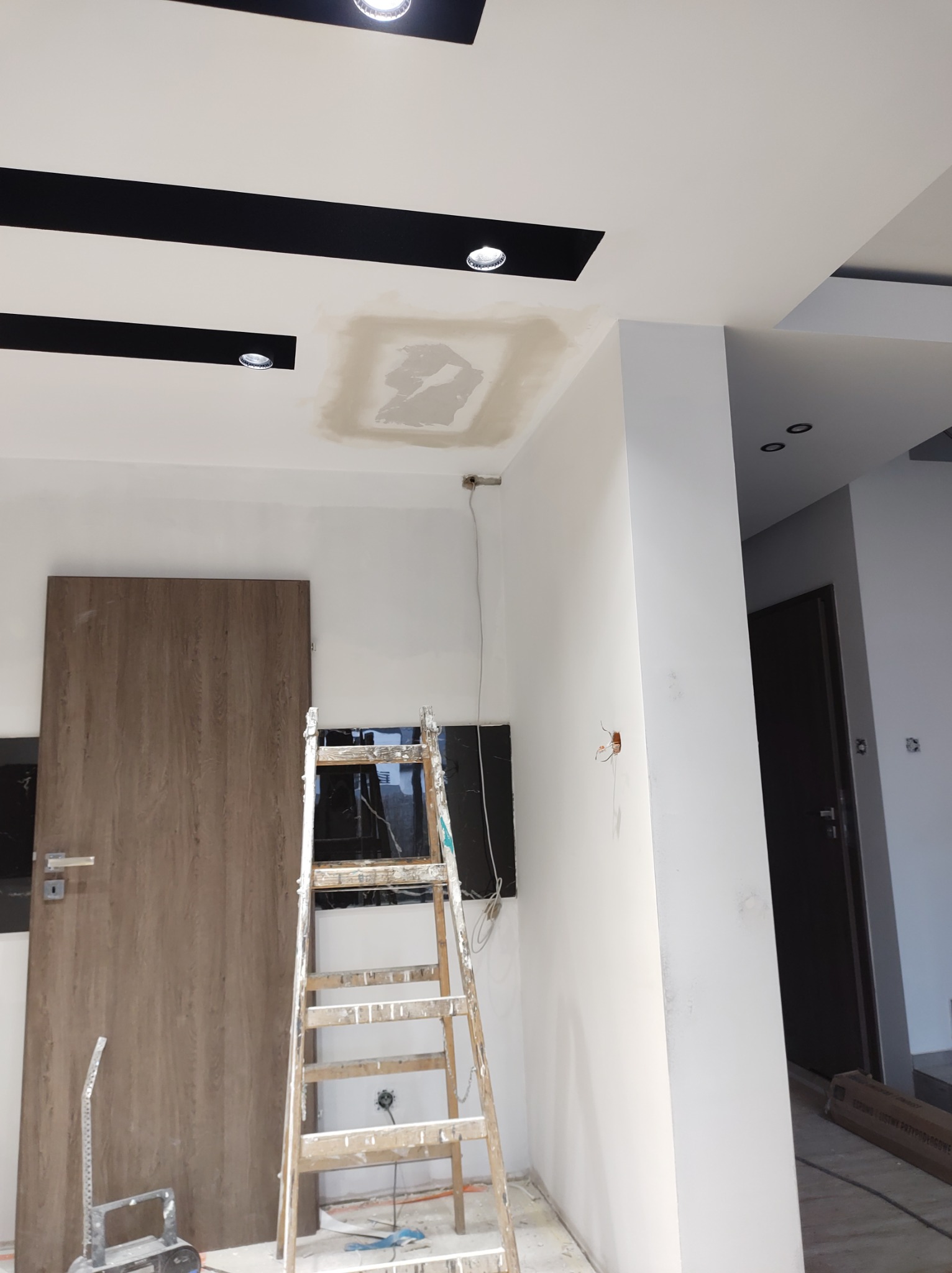 Szpachlowanie sufitu w trakcie remontu mieszkania, widoczna drabina malarska, ślady szpachli na suficie i niedokończone łączenie z oświetleniem punktowym.