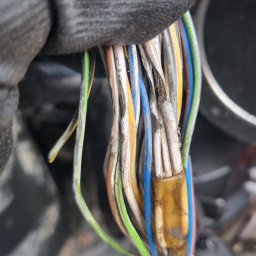 Diagnostyka I Maprawa Maszyn Budowlanych - Zbliżenie na wiązkę przewodów elektrycznych w rękawicy roboczej, z widocznymi uszkodzeniami izolacji i złączką.