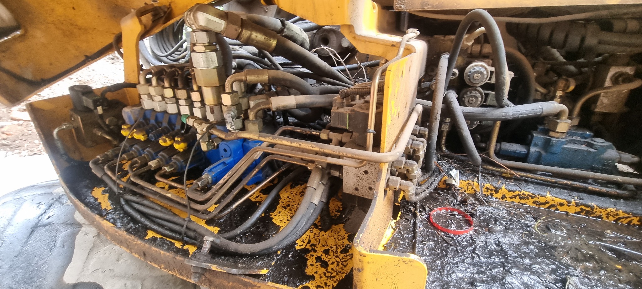 Wnętrze silnika żółtej maszyny budowlanej z widocznymi przewodami hydraulicznymi, zaworami i zabrudzeniami olejem.