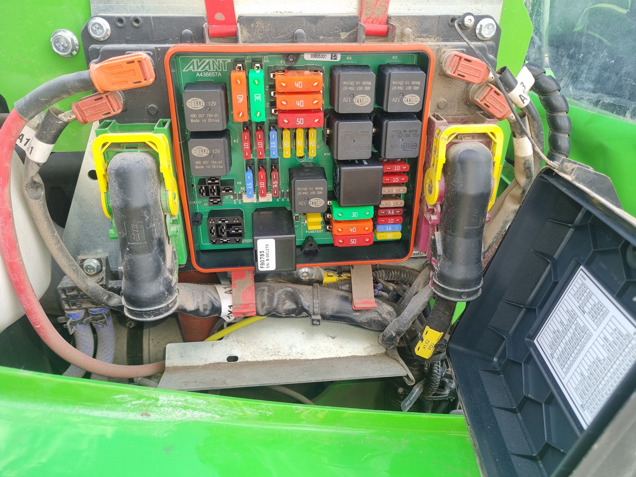 Otwarta skrzynka bezpieczników i przekaźników w maszynie marki Avant, widoczne kolorowe bezpieczniki o różnych wartościach amperażu i czarne przekaźniki Kella, przewody elektryczne z pomarańczowymi...