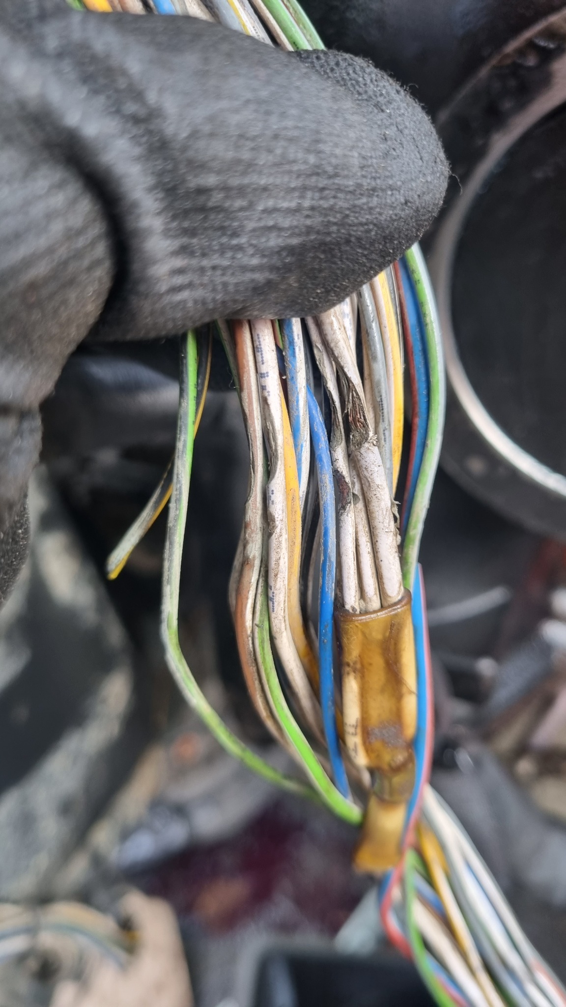 Zbliżenie na wiązkę przewodów elektrycznych w rękawicy roboczej, z widocznymi uszkodzeniami izolacji i złączką.