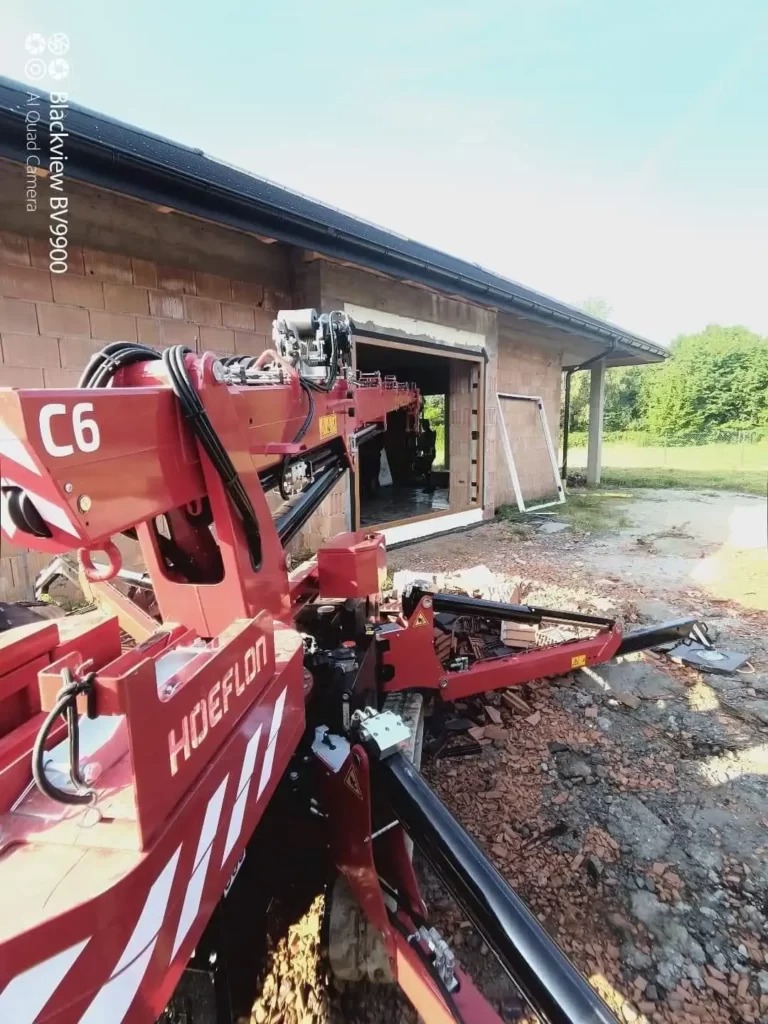 Montaż okna w Brzesku przy użyciu specjalistycznego dźwigu HOEFLON C6, widoczne przygotowane otwory okienne w surowym budynku z cegły.