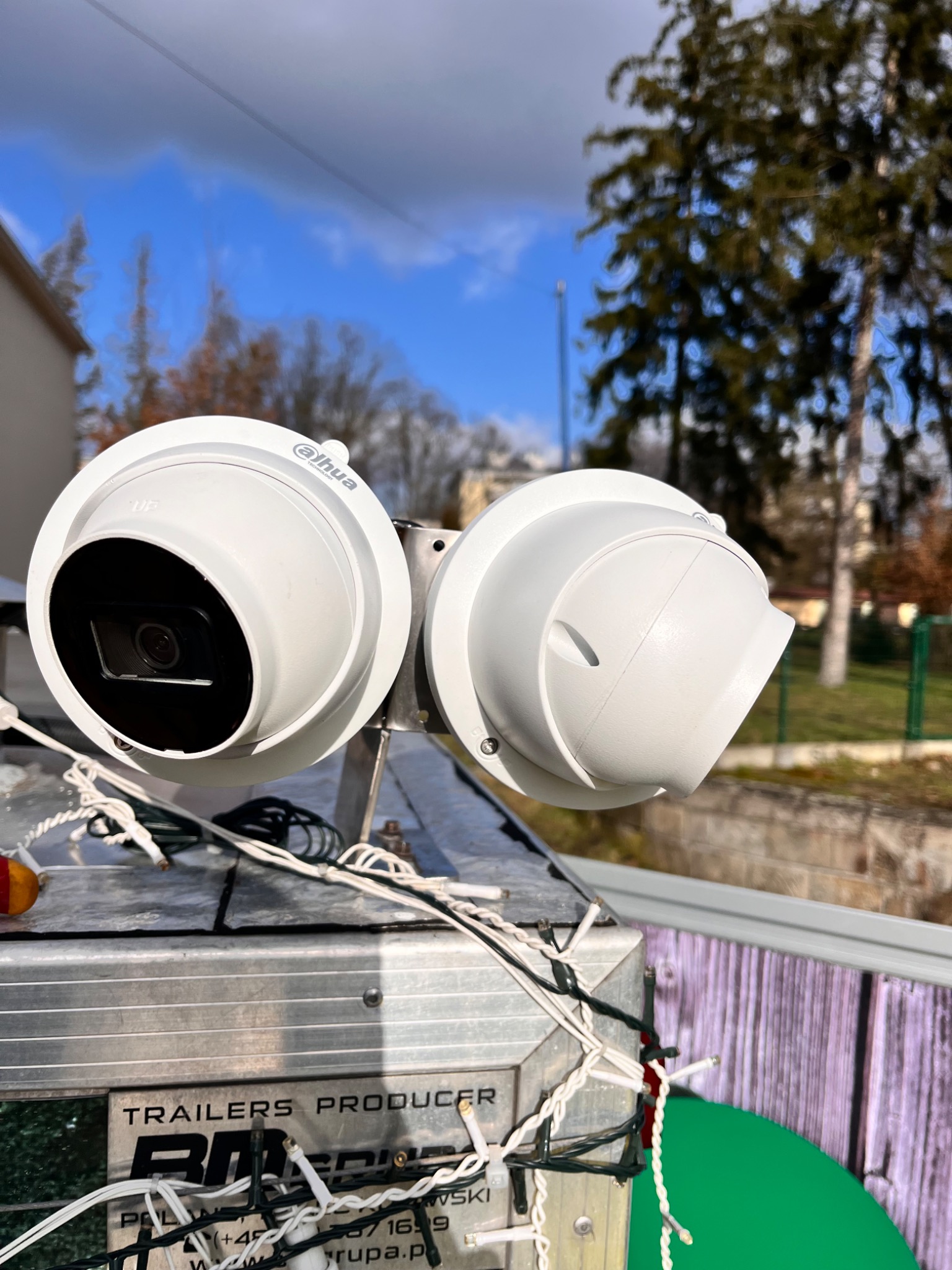 Dwie białe kamery monitoringu Dahua zamontowane na metalowej konstrukcji z widocznymi kablami na tle błękitnego nieba i drzew