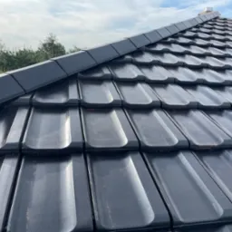 Nowy dach z czarnej dachówki ceramicznej w Kłobucku, widok z bliska na ułożone dachówki i obróbki blacharskie na krawędzi dachu, w tle zieleń drzew.
