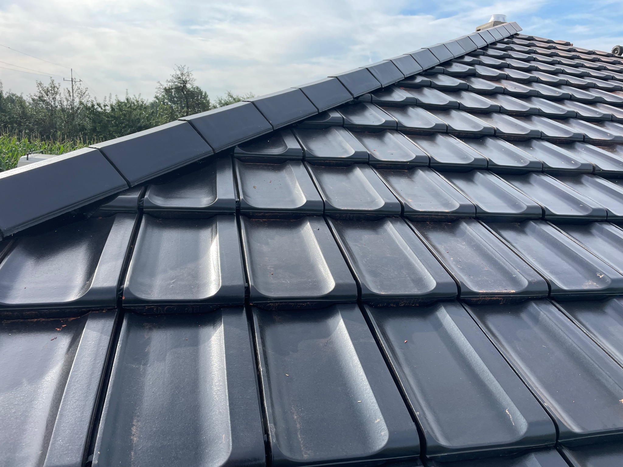 Nowy dach z czarnej dachówki ceramicznej w Kłobucku, widok z bliska na ułożone dachówki i obróbki blacharskie na krawędzi dachu, w tle zieleń drzew.