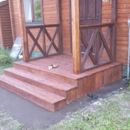 FRB JANICKI - Drewniany ganek z balustradą i trzema stopniami, świeżo po impregnacji. Widoczne detale drewnianej konstrukcji i otoczenie z zielenią.