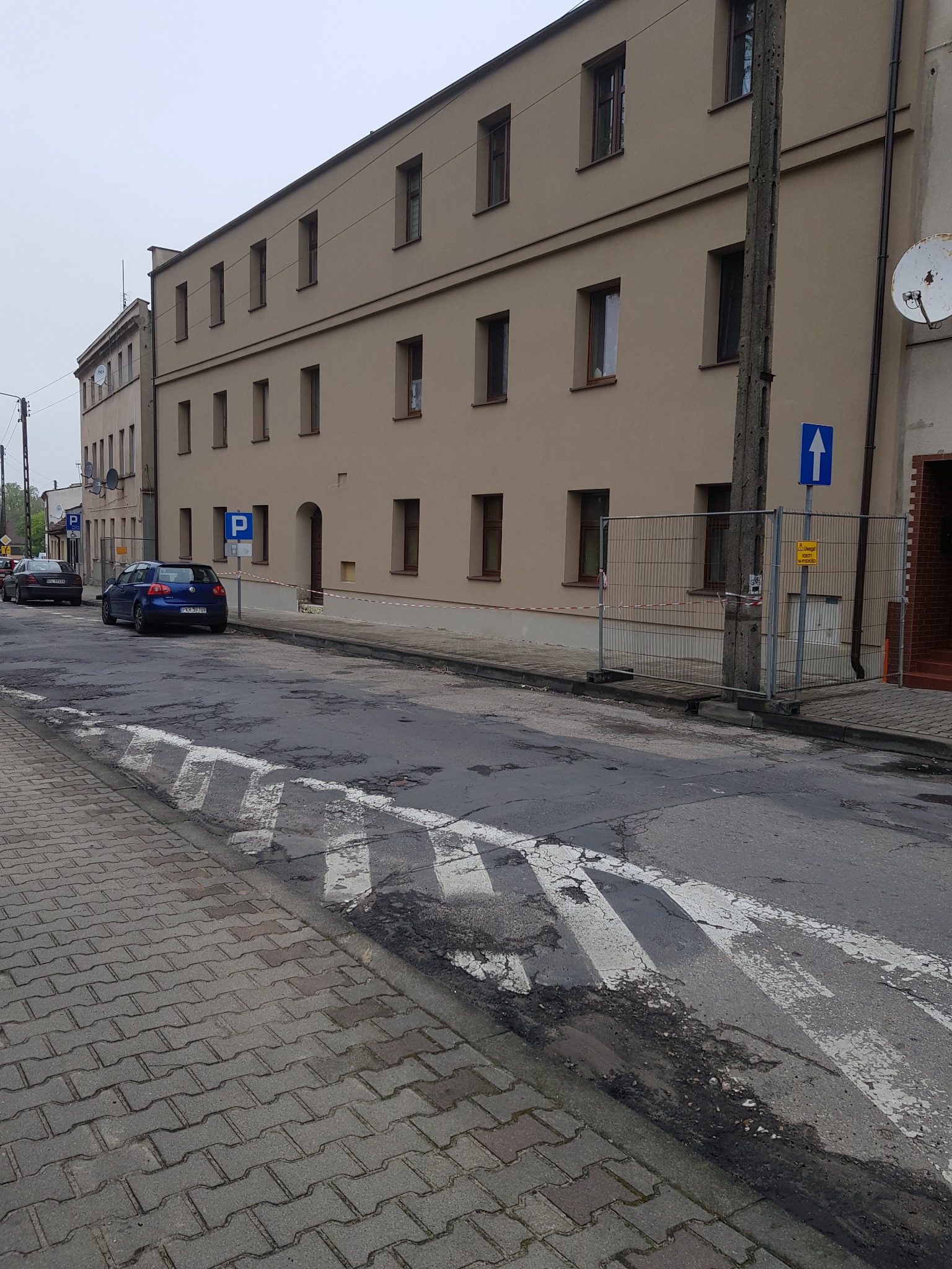 Elewacja kamienicy w trakcie remontu. Widoczne zabezpieczenia i uszkodzona nawierzchnia ulicy. Ujęcie z poziomu chodnika.