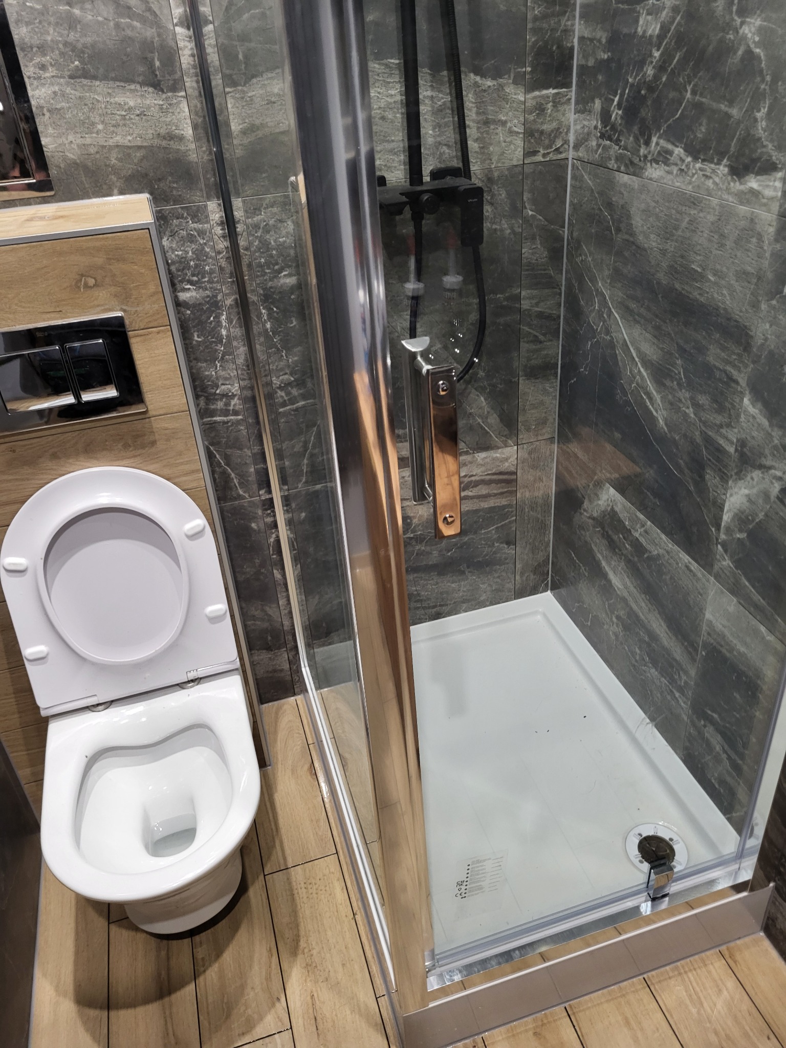 Nowoczesna łazienka z kabiną prysznicową typu walk-in, toaletą podwieszaną i marmurowymi płytkami na ścianach.