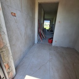 Łukasz Hyrchel - Wnętrze w trakcie prac: ułożone płytki podłogowe i ścienne imitujące marmur. Widoczne narzędzia, surowe ściany i otwór drzwiowy w stanie wykończeniowym.