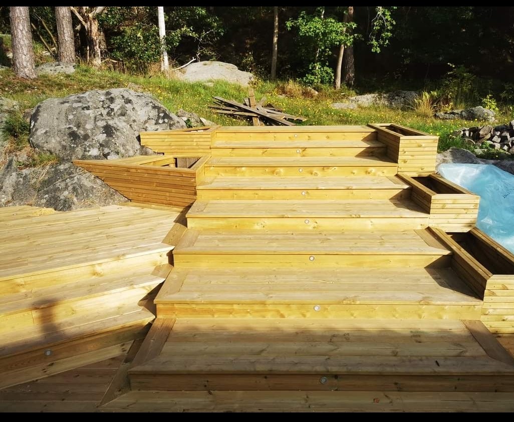 Drewniane schody tarasowe z wbudowanymi donicami na tle naturalnego ogrodu ze skałami i drzewami.