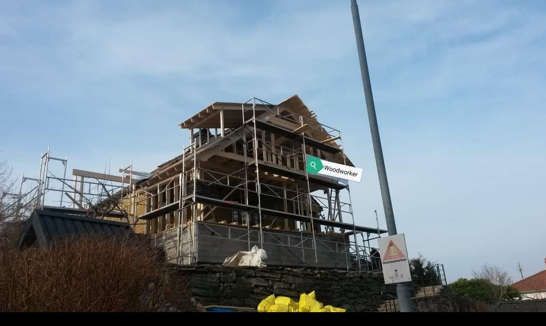 Wznoszenie drewnianej konstrukcji domu w trakcie budowy, widoczne rusztowania i częściowo zamontowane ściany.