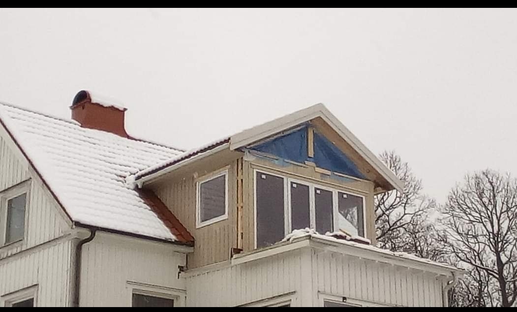 Rozbudowa domu z widoczną konstrukcją dachu, oknami wstawionymi w nową część oraz śniegiem na dachu i tle drzew bez liści.