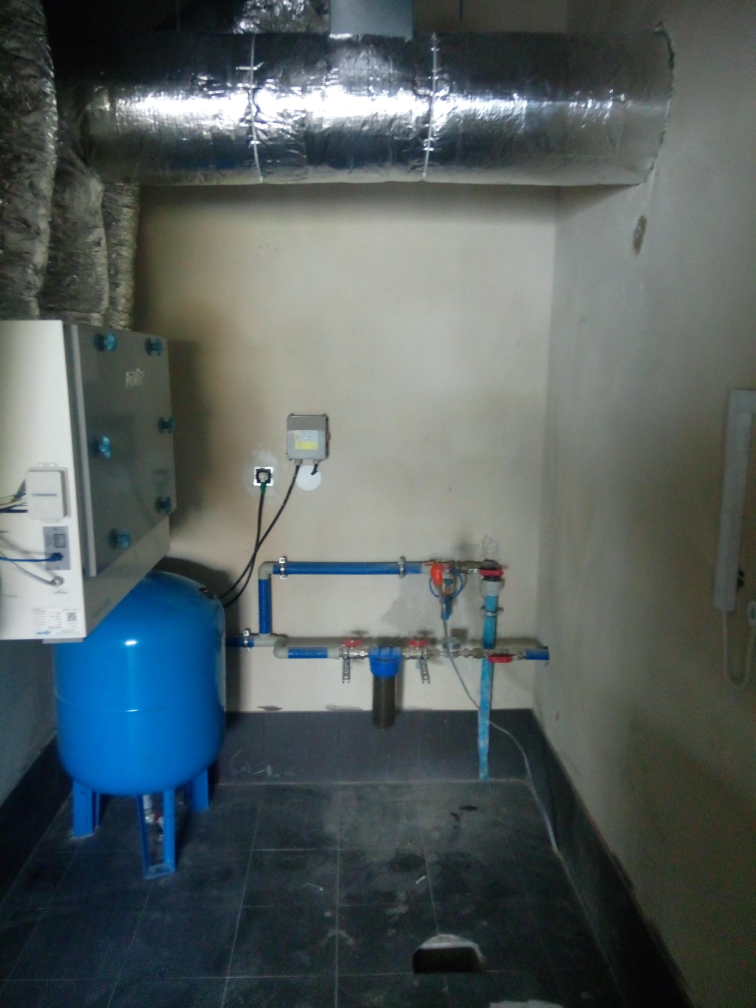 Wnętrze kotłowni z rekuperatorem, niebieskim zbiornikiem ciśnieniowym, systemem rur i przewodami wentylacyjnymi obłożonymi folią aluminiową.