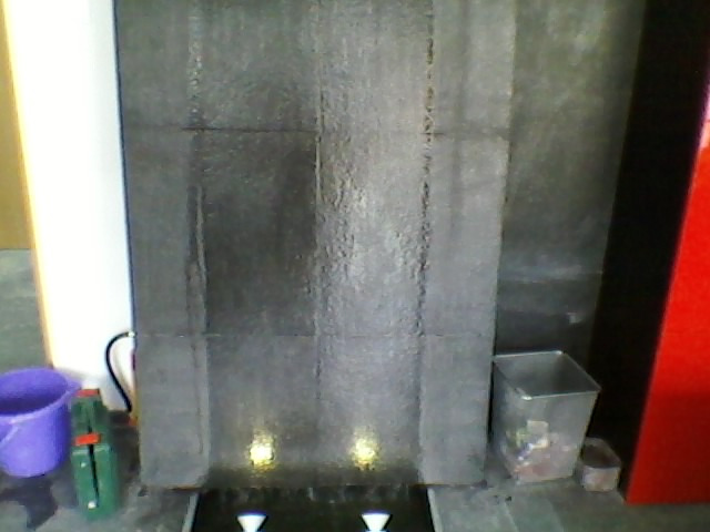 Tekstura ściany z efektem wodospadu, podświetlona od dołu, widoczne narzędzia i wiadro w pobliżu.