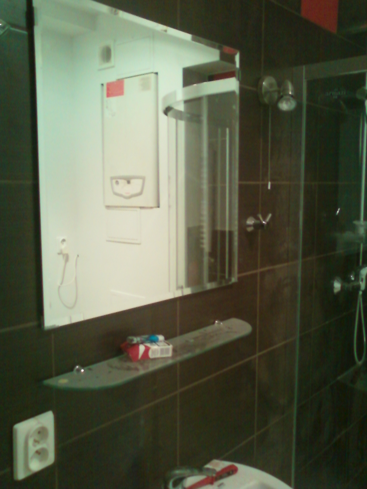 Ukończona łazienka z ciemnymi płytkami, kabiną prysznicową i lustrem, w którym odbija się piec gazowy.