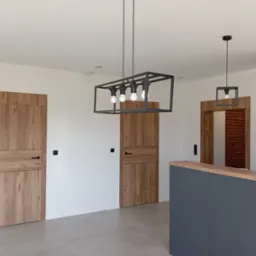 Wnętrze z dwiema drewnianymi drzwiami z poziomymi panelami, nowoczesnym oświetleniem i szarą zabudową. Widok na ceglaną ścianę przez otwarte drzwi.