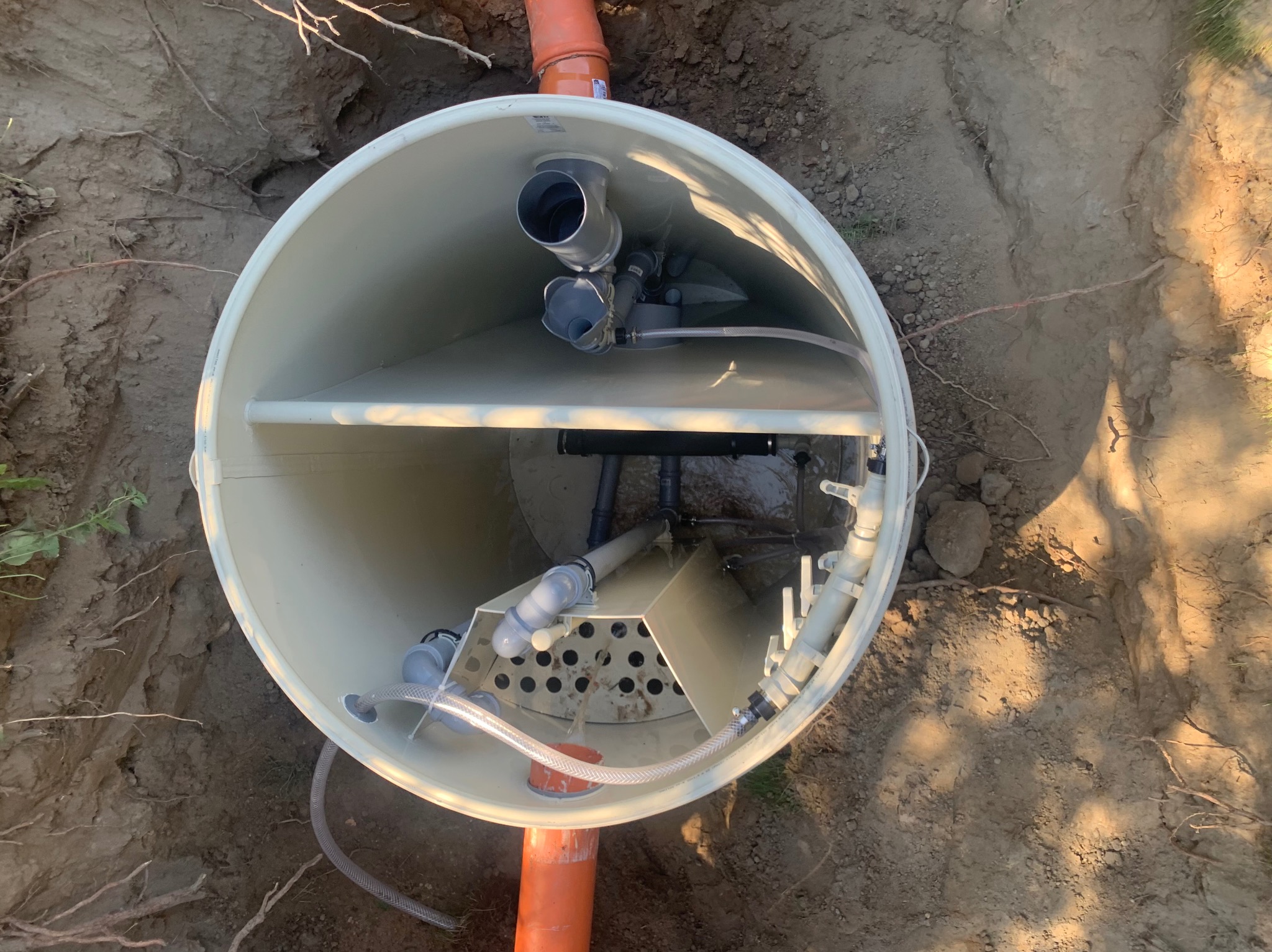 Wnętrze zbiornika przydomowej oczyszczalni ścieków w wykopie, widoczne rury i elementy instalacji, górny widok.