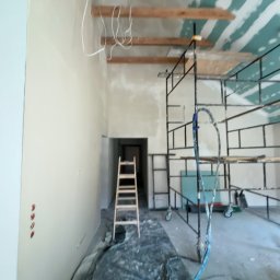 Mateusz Antczak - Wnętrze w trakcie remontu: ściany po szpachlowaniu, widoczne przewody elektryczne pod sufitem, rusztowanie i drabina. Przygotowanie do dalszych prac wykończeniowych.
