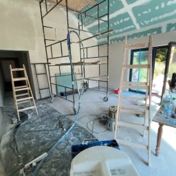 Mateusz Antczak - Wnętrze w trakcie szpachlowania: widoczne rusztowanie, drabina, narzędzia i częściowo wykończone ściany z płyt gipsowo-kartonowych. Detal: pojemnik z napisem 'Mycie maszyn'