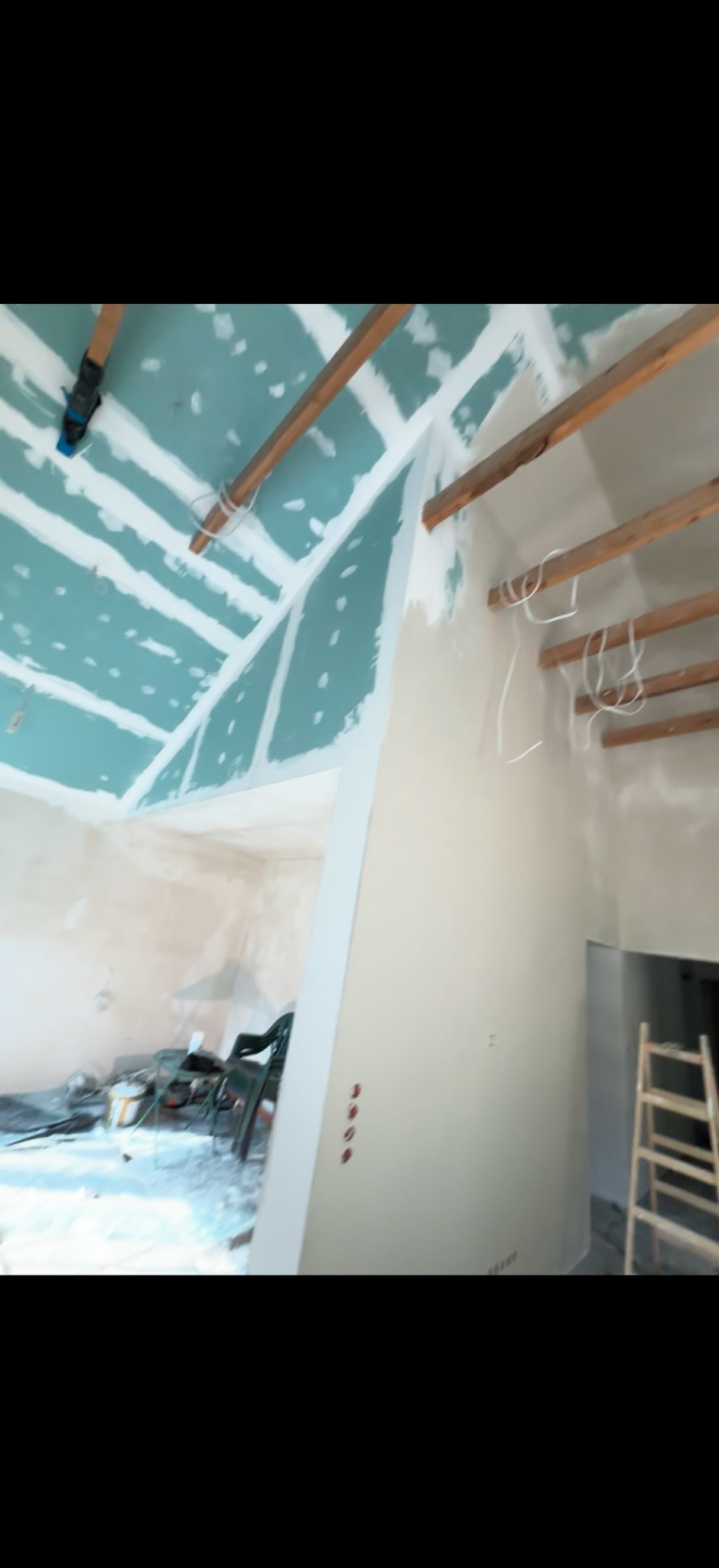 Wnętrze w trakcie remontu: sufit z płyt gipsowo-kartonowych na drewnianej konstrukcji, częściowo otynkowane ściany, drabina i narzędzia w tle. Prace wykończeniowe.