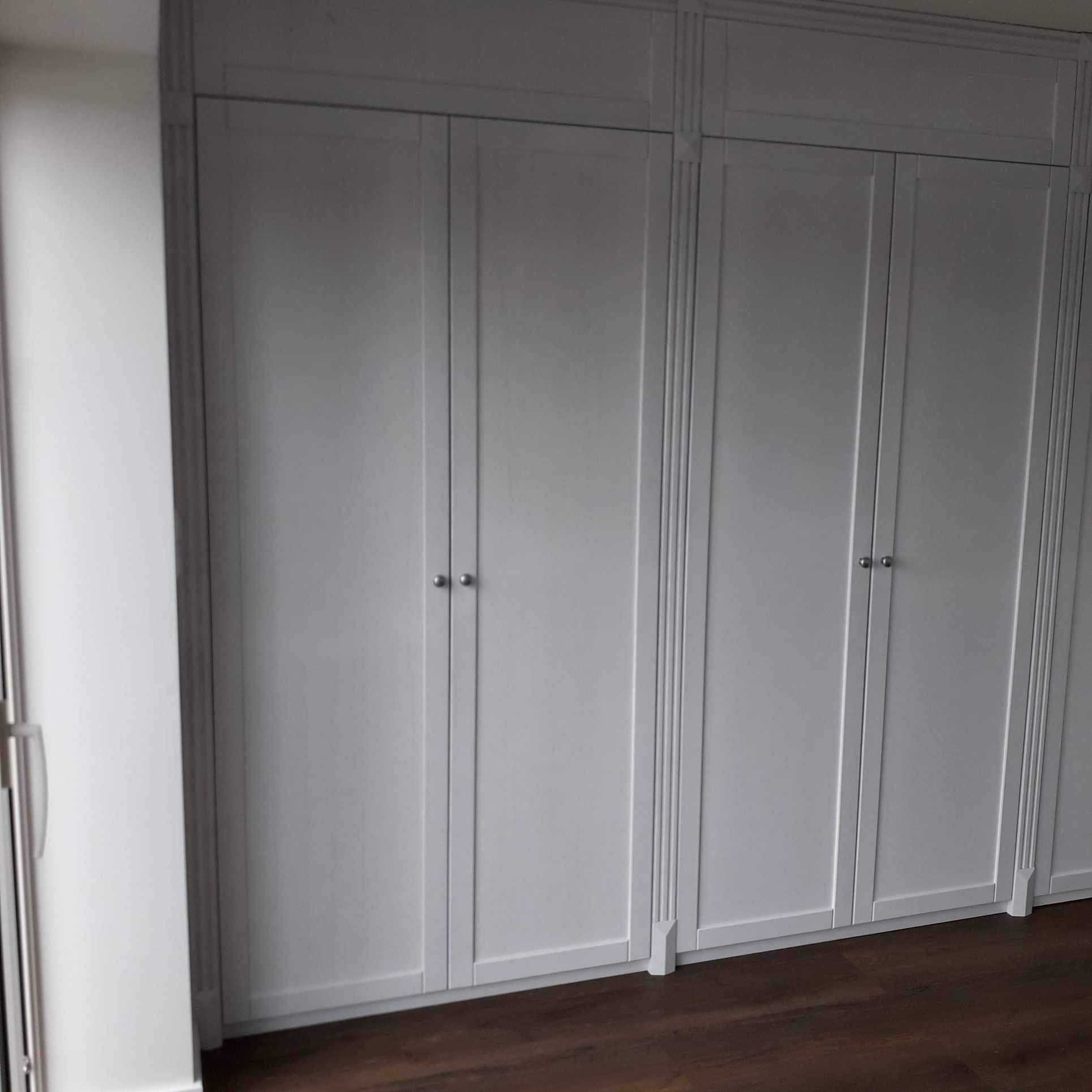 Wbudowana szafa z białymi drzwiami panelowymi i srebrnymi gałkami, wykonana na wymiar w Ostródzie, widoczna na tle ciemnej drewnianej podłogi.