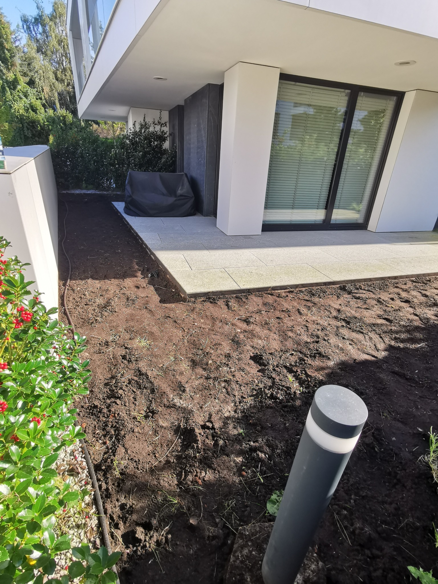 Przygotowany teren pod budowę tarasu przy nowoczesnym domu z widocznymi płytami tarasowymi i elementami oświetlenia ogrodowego.