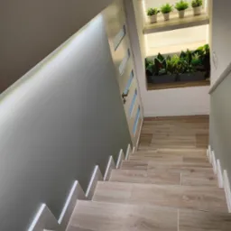 Schody wyłożone płytkami imitującymi drewno, z dekoracyjną wnęką oświetloną LED z roślinami doniczkowymi na dwóch poziomach.