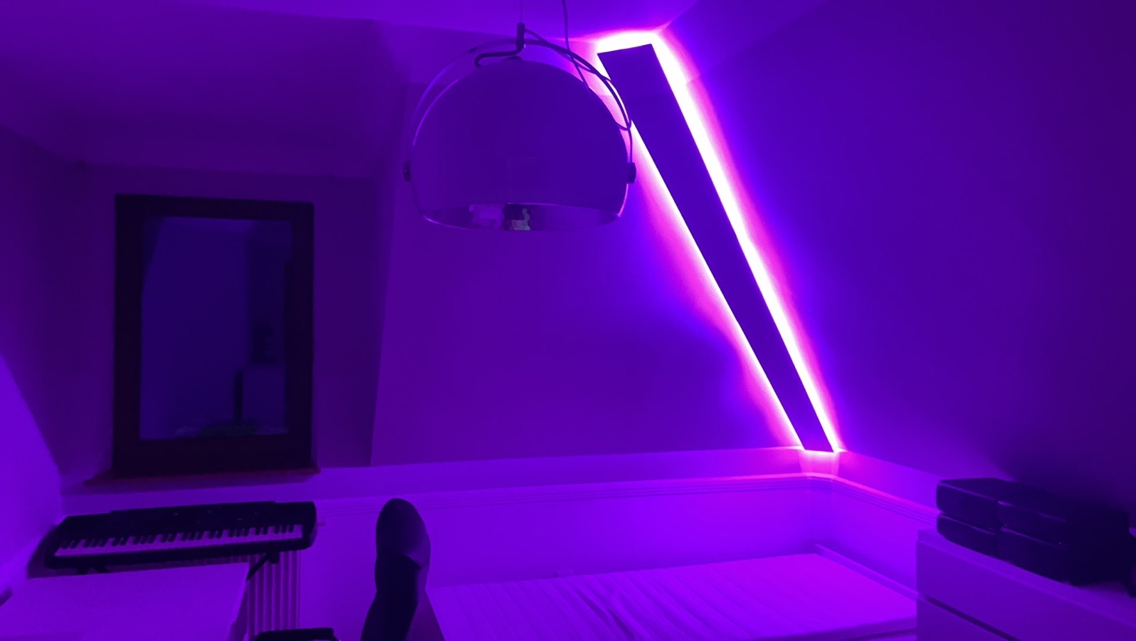 Pokój na poddaszu oświetlony fioletowymi LED-ami RGB, z widocznym łóżkiem, lampą wiszącą i klawiaturą muzyczną.