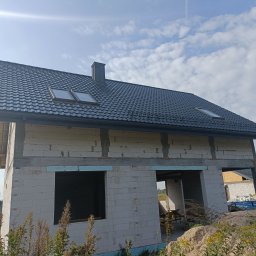 Twój Dach - Dom w trakcie budowy z ciemnoszarą dachówką, widoczne okna dachowe i komin, ściany z betonu komórkowego w stanie surowym otwarte, nieotynkowane.