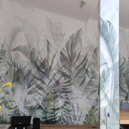 Art Life - Jasne wnętrze z fototapetą w motywy roślinne, stół z krzesłami w tle, widok na kuchnię z oknem w oddali.