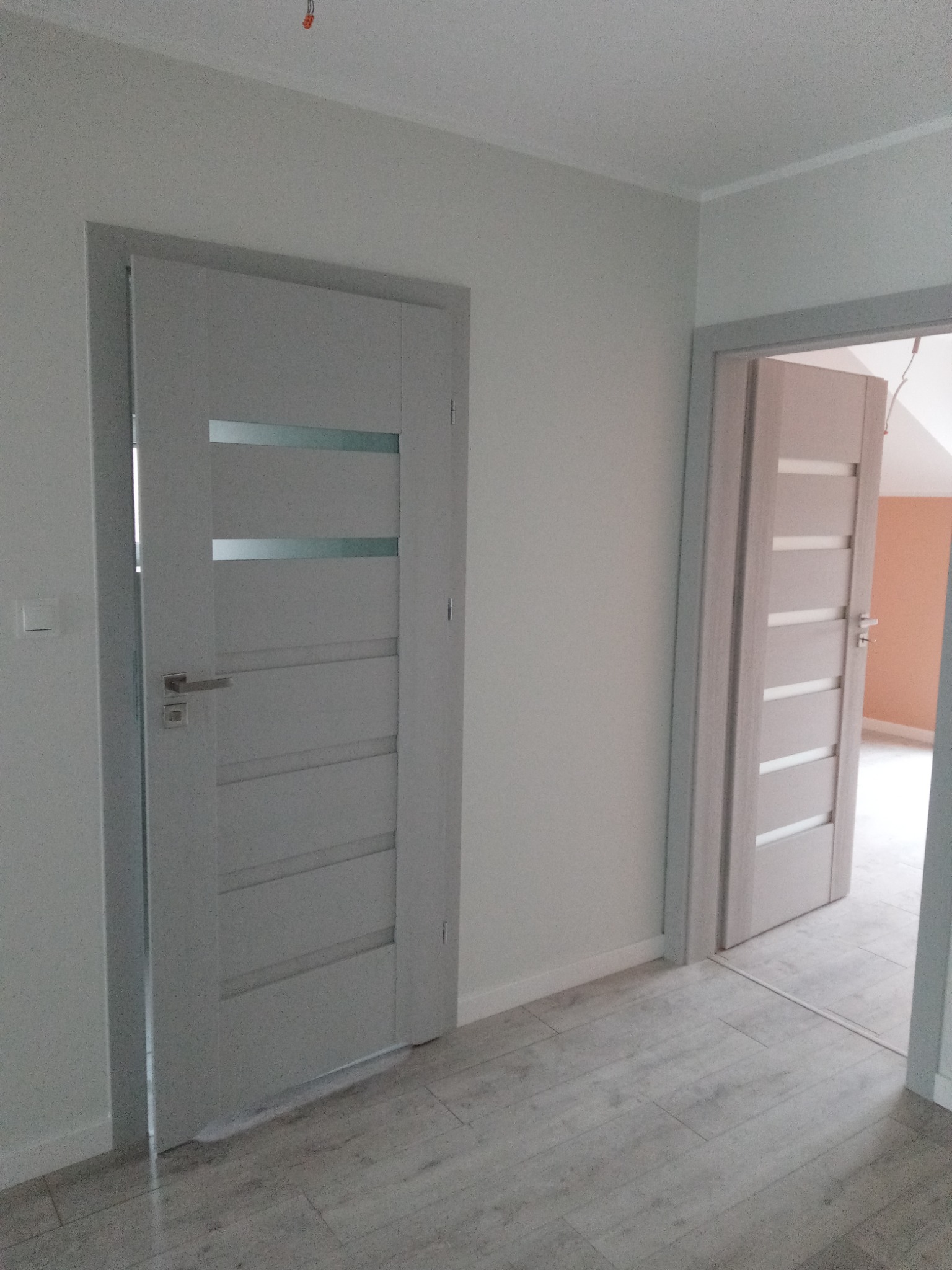 Dwa szare, nowoczesne drzwi wewnętrzne z poziomymi przeszkleniami, zamontowane w odnowionym mieszkaniu, widoczne panele podłogowe w odcieniach szarości.